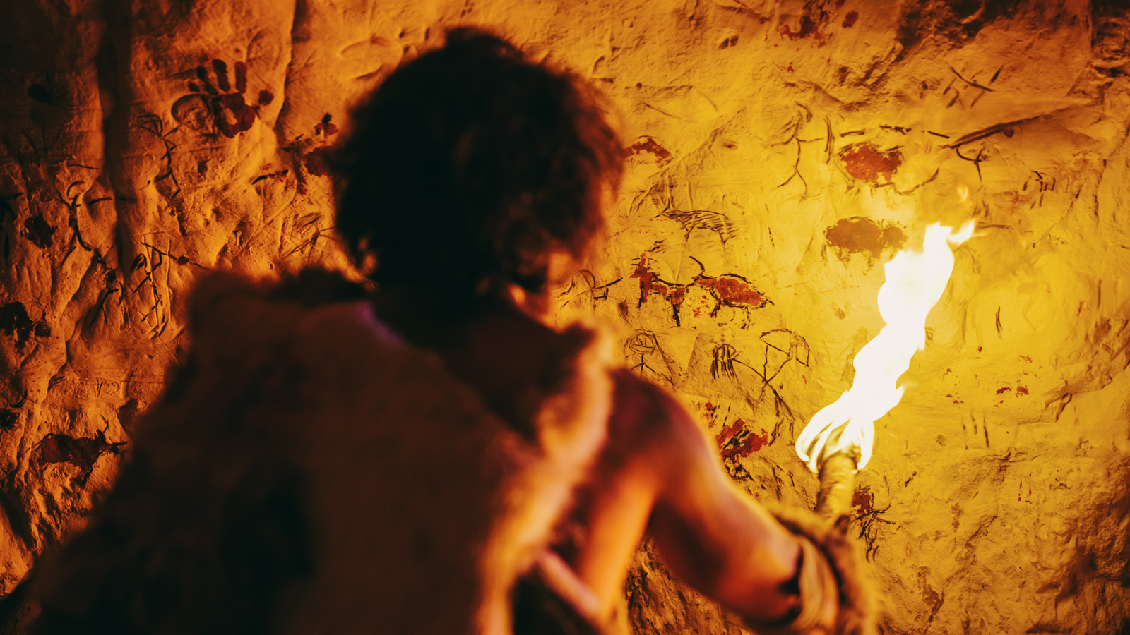 Frühmensch in Höhle mit Fackel vor Höhlenmalerei